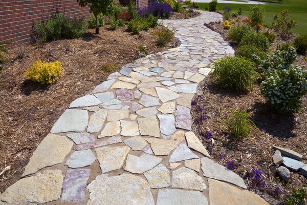 Flagstone garden walkway installed with natural stone pavers and edging through landscaped beds